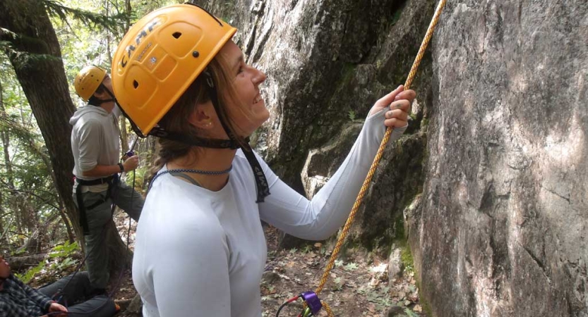 Two people wearing yellow helmets and other safety gear belay climbers